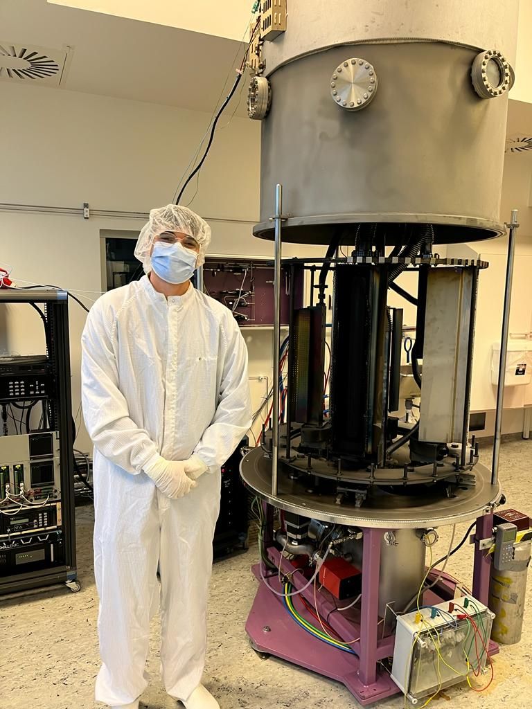 Francisco in a cleanroom suit next to the optics coating chamber at DTU Space